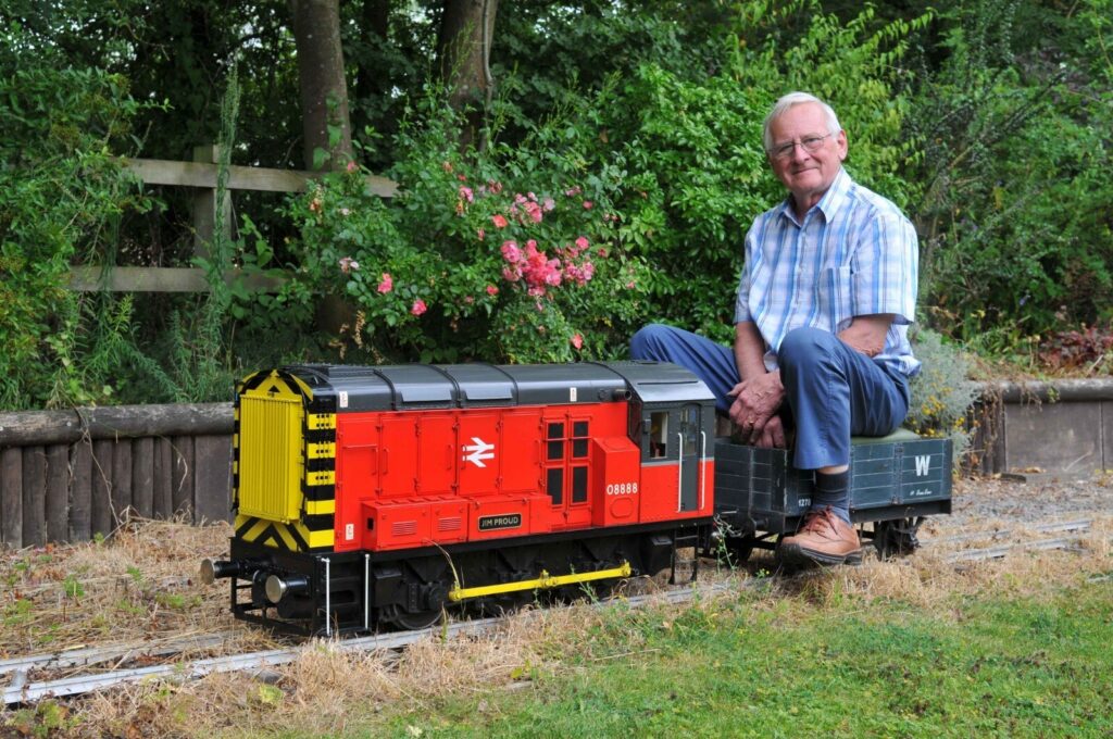 Richard sitting on his model train in his garden