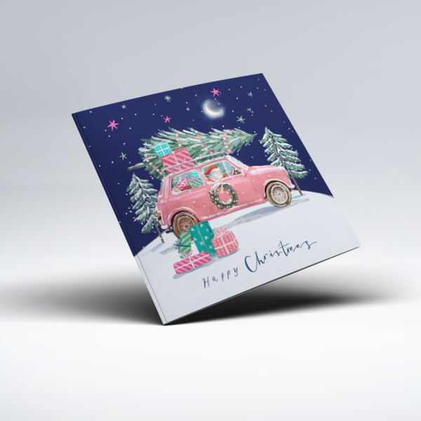 Colourful illustrated Christmas card showing Father Christmas driving a bright red car through a snowy winter scene, with a Christmas tree and wrapped presents secured to the roof. Colourful gifts sit in the snow beside the car, surrounded by fir trees beneath a dark blue sky filled with stars and a crescent moon, with the words "Happy Christmas" below.