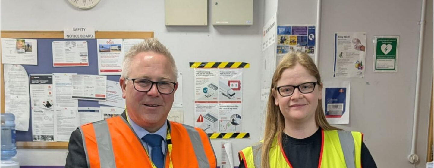 GXO Logistics staff stand either side of a framed and signed Doncaster Rovers FC shirt.