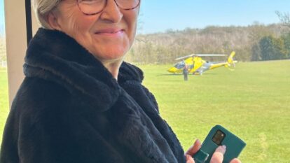 Woman smiling wearing black coat with window and helicopter in background
