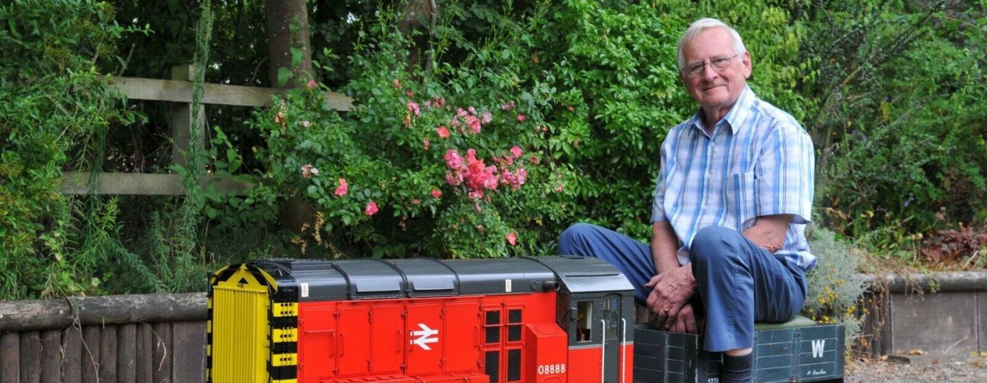 Richard sitting on his model train in his garden