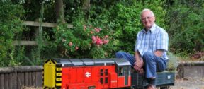 Richard sitting on his model train in his garden