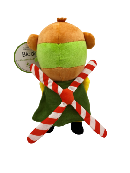 Rear facing photograph of stuffed bear plush, Blade - our TCAA mascot. He's wearing a yellow top, and a green cape and mask. On his back are helicopter blades, which can be clearly seen from this angle.