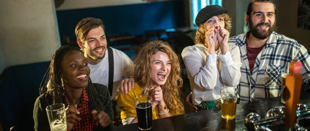 4 young people watching sports in a bar smiling
